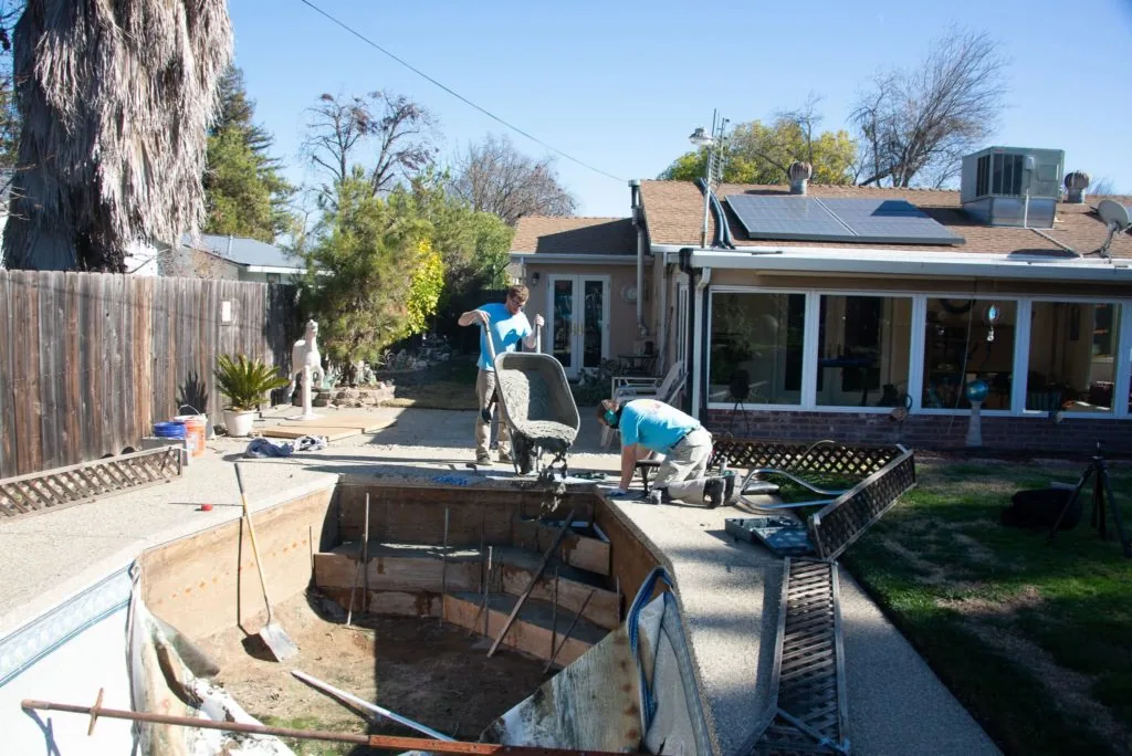 Residential backyard with wooden deck, blue construction equipment, metal trailer, and house with solar panels