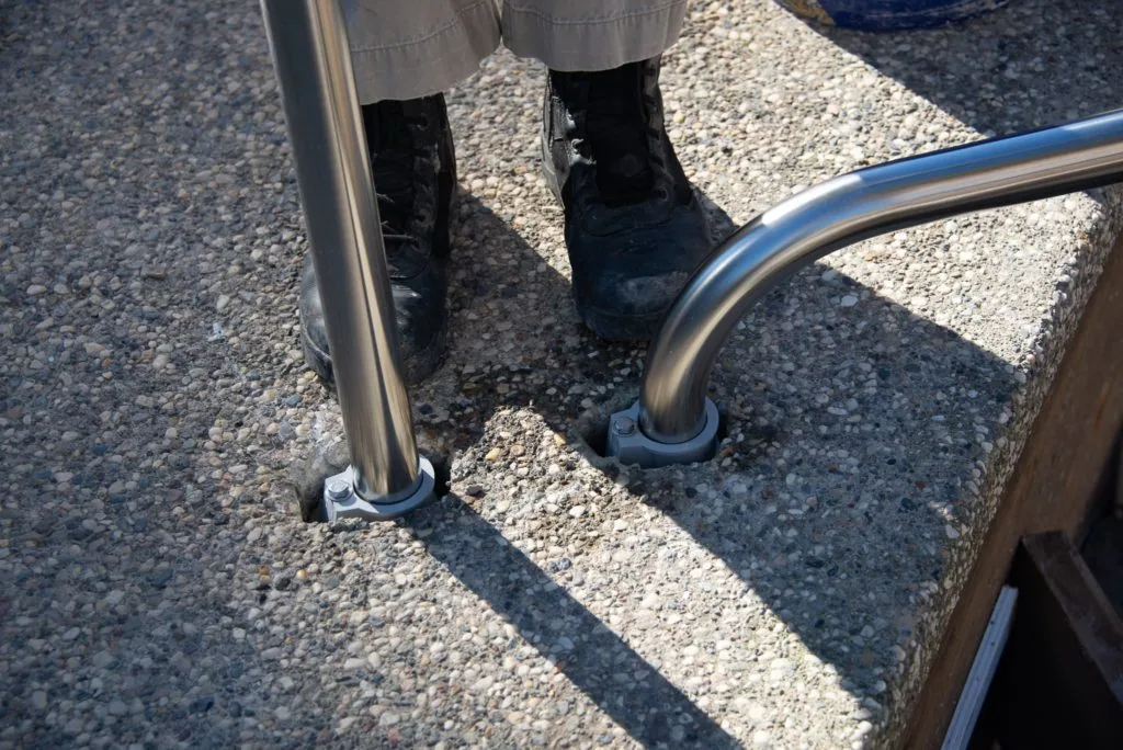 Person wearing black boots standing on gravel surface next to metal railing posts