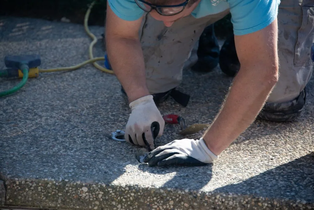 Worker in protective gloves and blue shirt smoothing concrete surface during pool construction