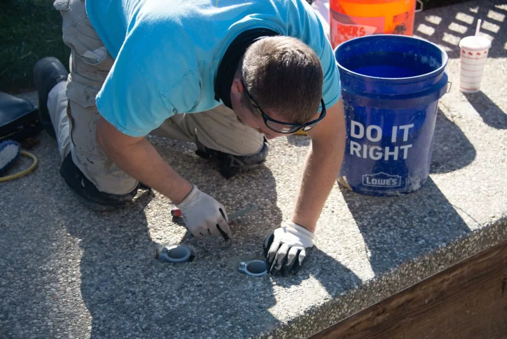 Person in blue shirt applying sealant or coating to concrete pool deck surface with a blue bucket nearby