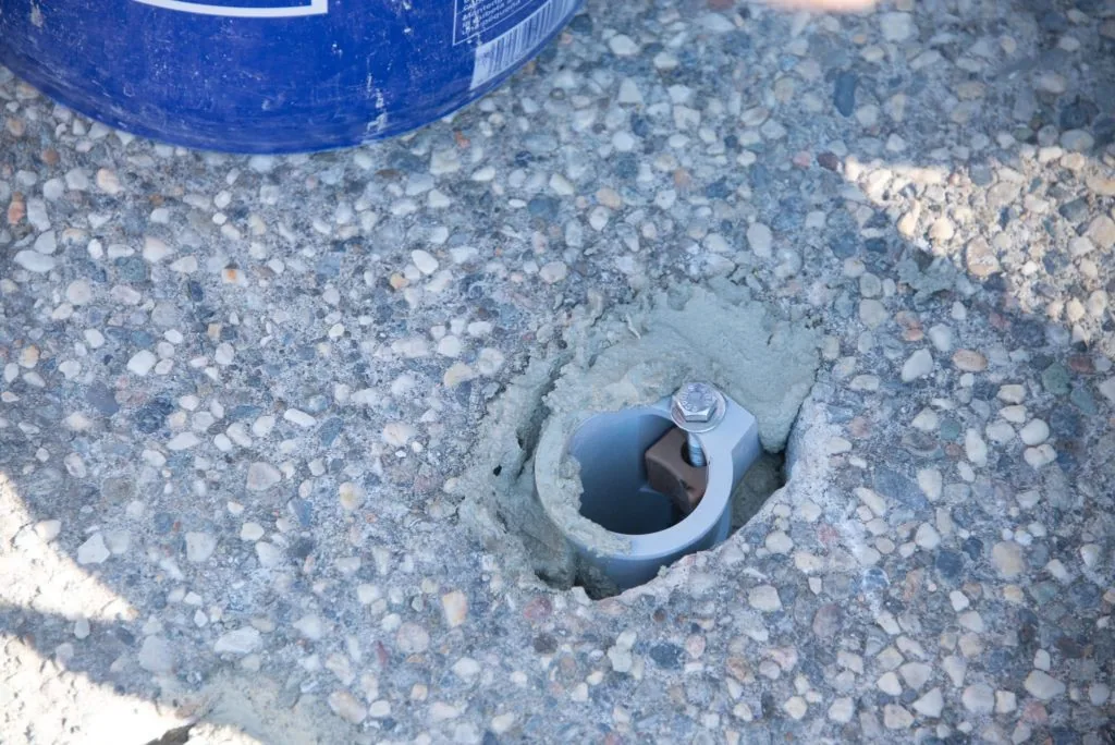 Metal anchor bolt with nut embedded in gravel near blue pool equipment