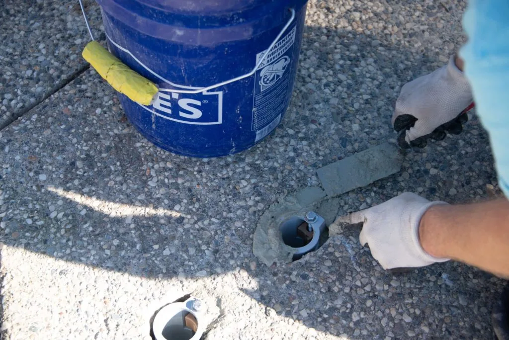 Blue bucket with yellow handle next to pool drain pipes and valves on concrete surface