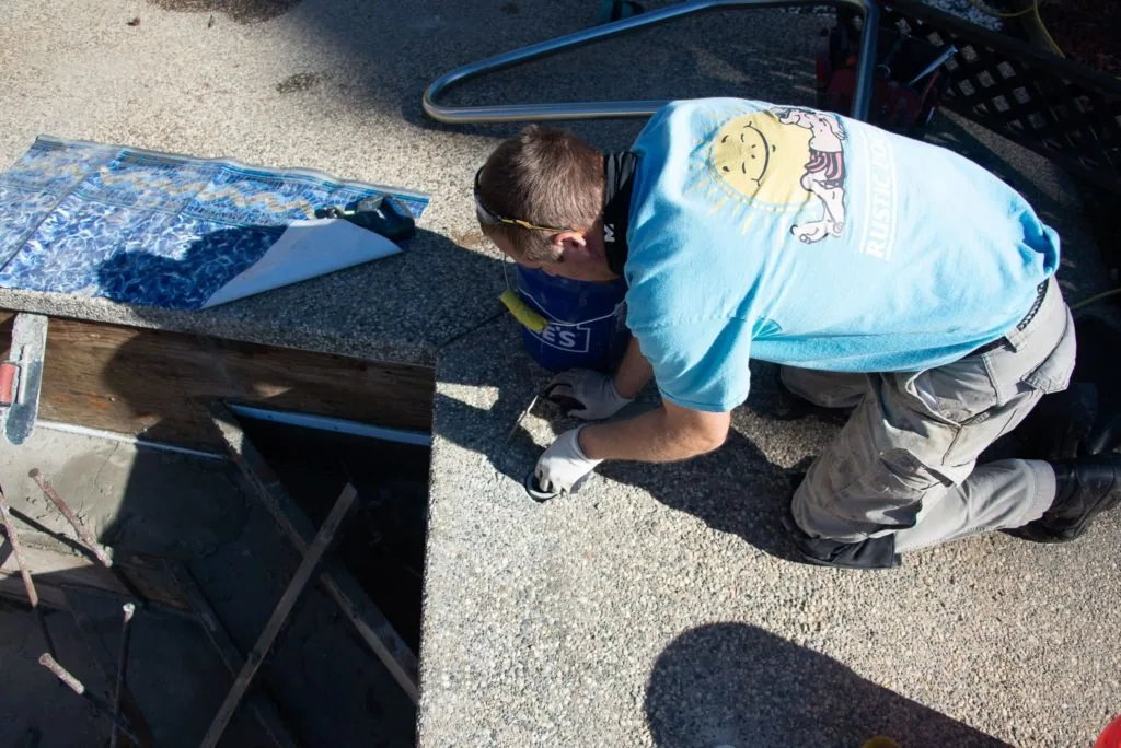 Child in light blue shirt crouching on concrete surface next to swimming pool equipment and supplies