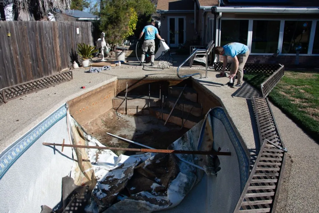 Workers in blue shirts draining and cleaning an empty residential swimming pool in a backyard.