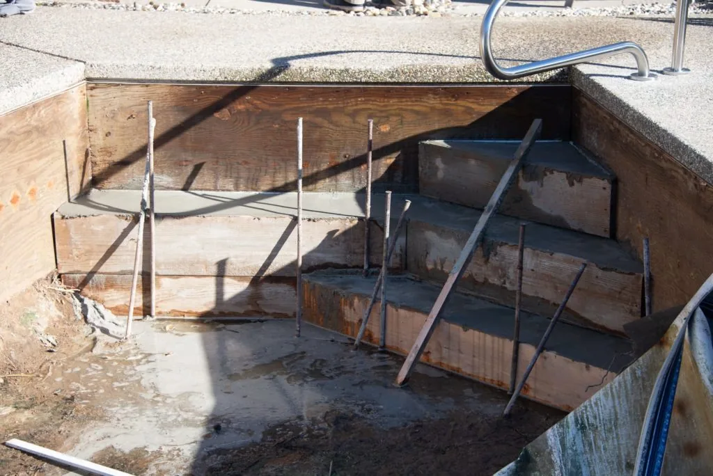 Wooden pool structure under construction with metal support posts and blue pipes