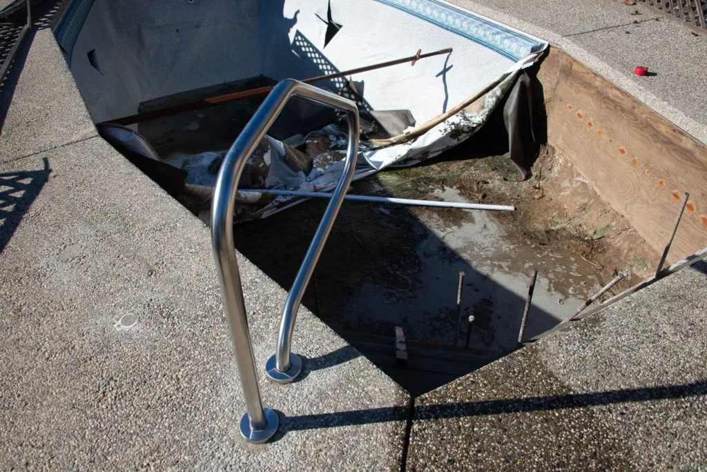 Damaged black metal boat with broken frame and blue pipes lying on concrete pavement next to wooden barrier