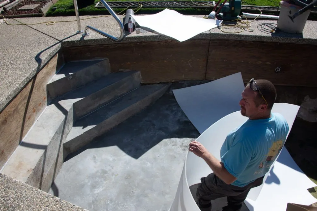 Man in blue shirt inspecting interior of concrete pool under construction with metal beams and white covering