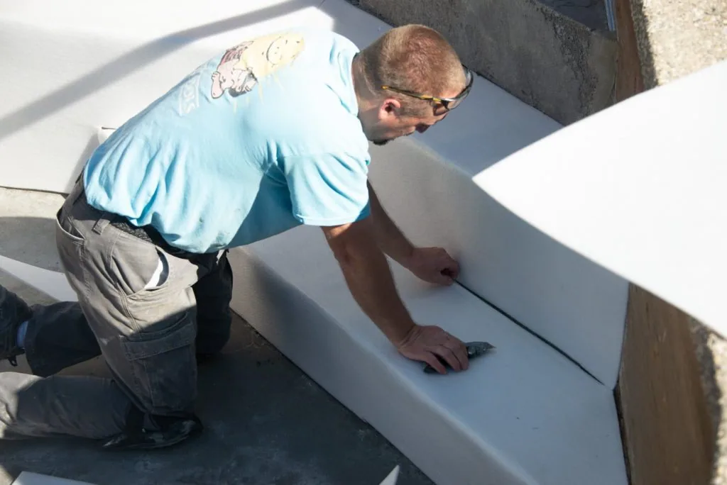 Worker in blue shirt kneeling and smoothing white material on pool surface