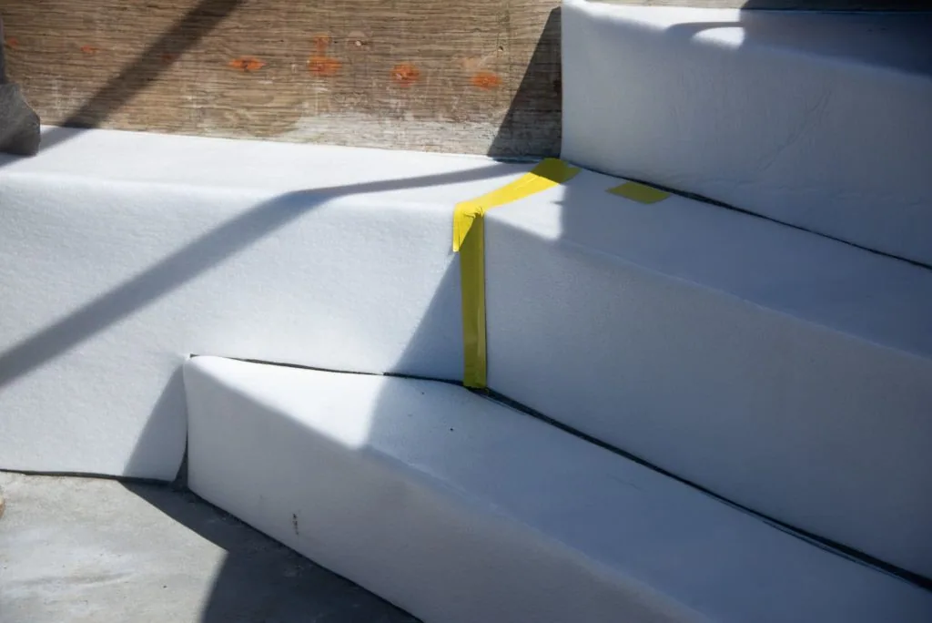 Stacked white foam insulation boards with yellow spacer strip on concrete surface against brick wall