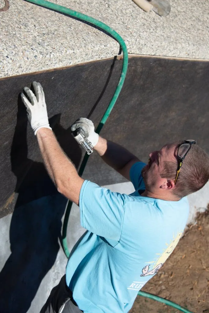 Worker in light blue shirt and white gloves installing or adjusting green hose on dark pool surface