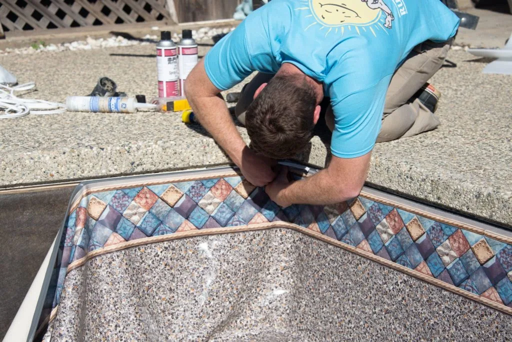 Person in blue shirt installing decorative tile border on swimming pool edge