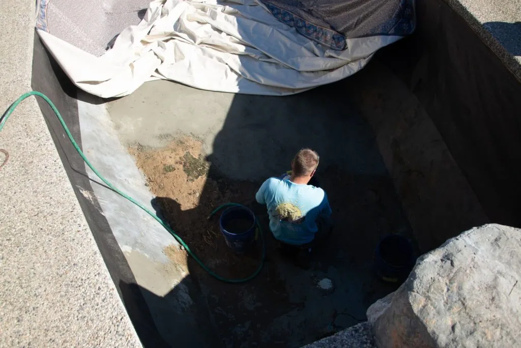 Person in blue shirt working in deep excavated pit with hose and bucket