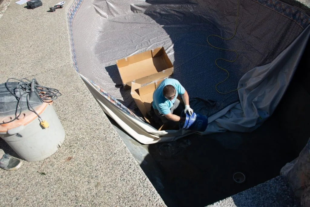 Person standing in empty swimming pool holding cardboard box during daytime