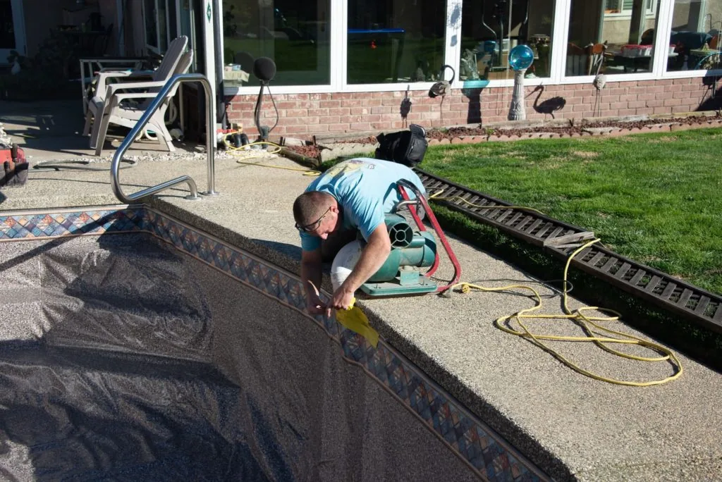 Man installing or repairing dark patterned pool liner in residential pool area with equipment nearby