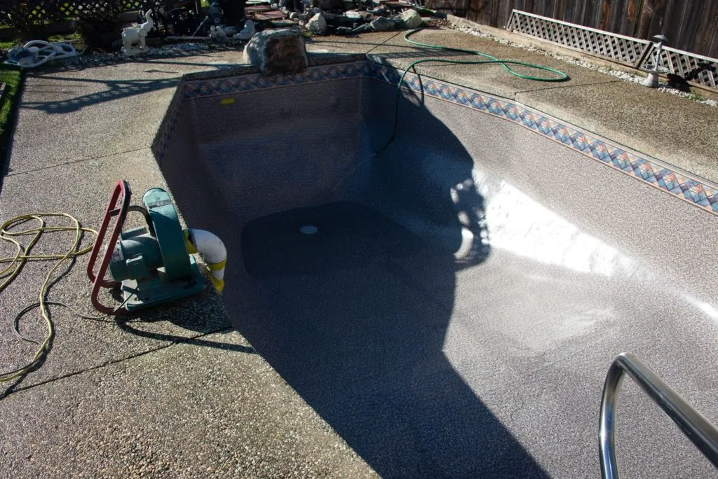 Empty pool being drained with hoses and equipment on deck during daytime maintenance