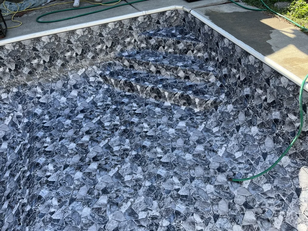 Rectangular pool filled with gray crushed stone or pebble interior, white trim edge, green hose visible above