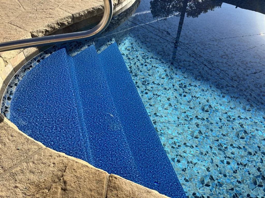 Overhead view of residential swimming pool with blue tile and pebble finishes, concrete deck, and surrounding landscape