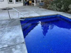 In-ground swimming pool with bright blue tile interior and metal ladder beside concrete deck