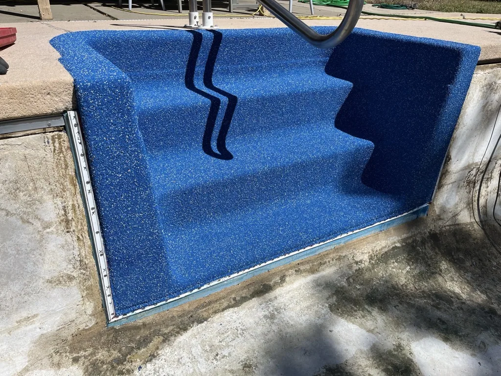 Empty swimming pool with blue textured interior surface and black drainage pipe