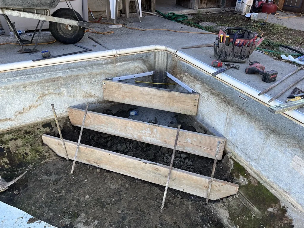 Wooden boat frames sitting inside a concrete pool structure under construction at a work site