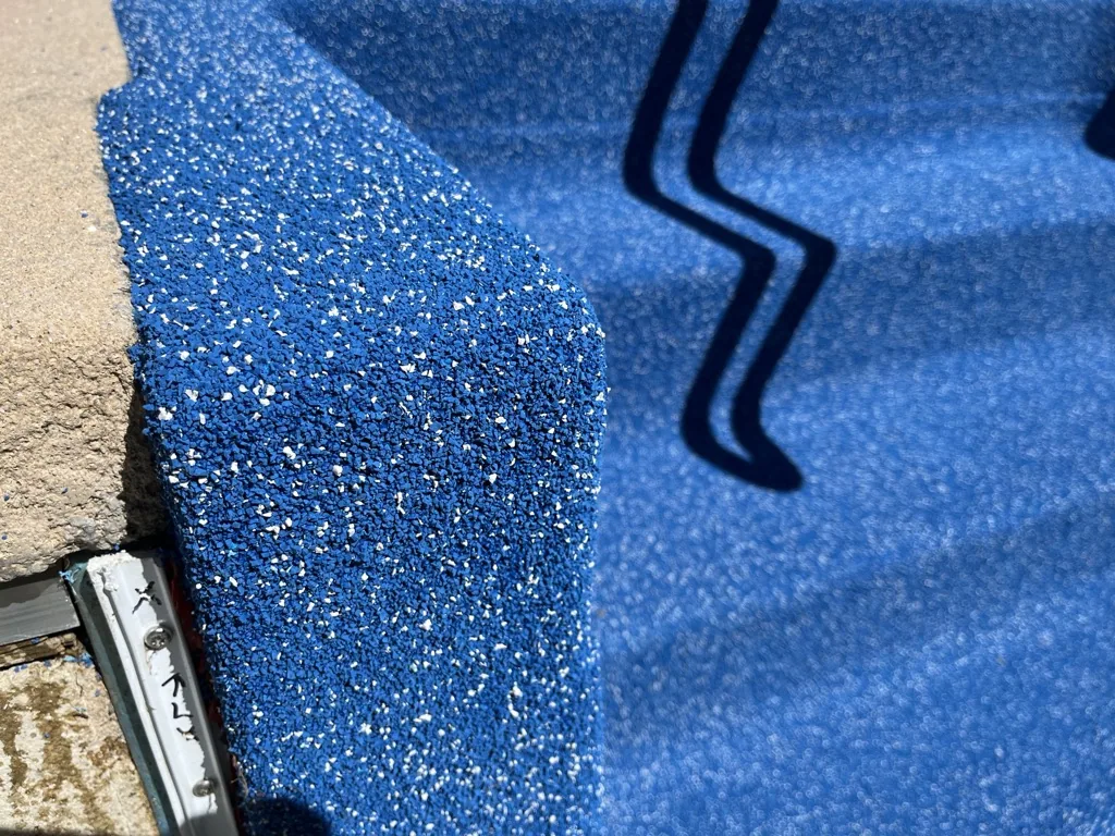 Blue pool liner with glittery texture meeting concrete deck edge and dark curved trim