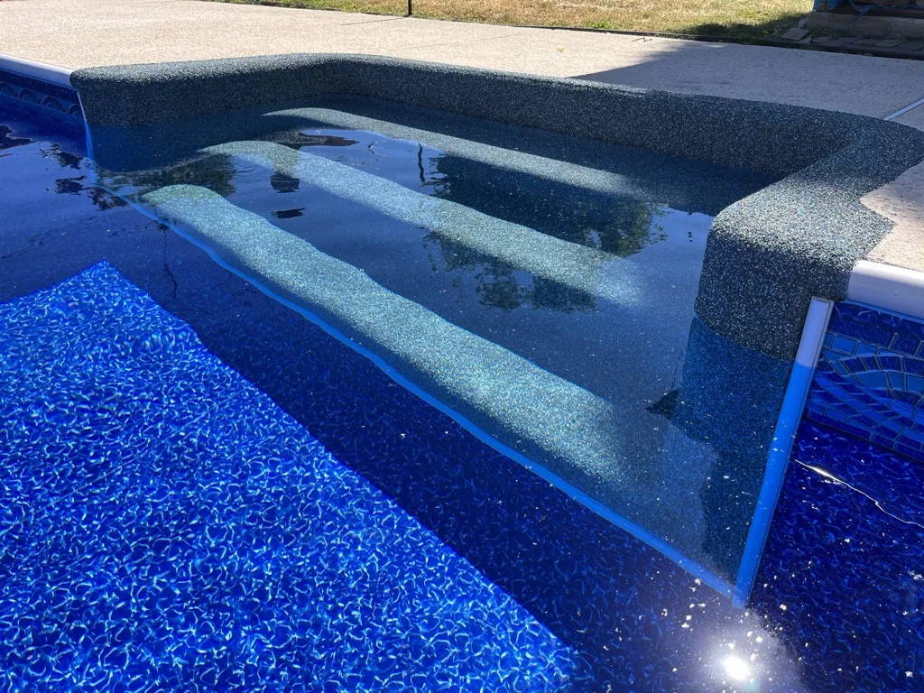 Swimming pool with built-in concrete bench seating and blue mosaic tile lining