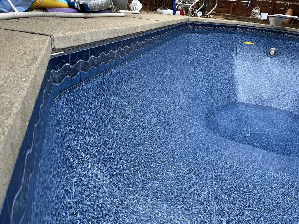 Empty swimming pool with blue mosaic tile interior and concrete deck