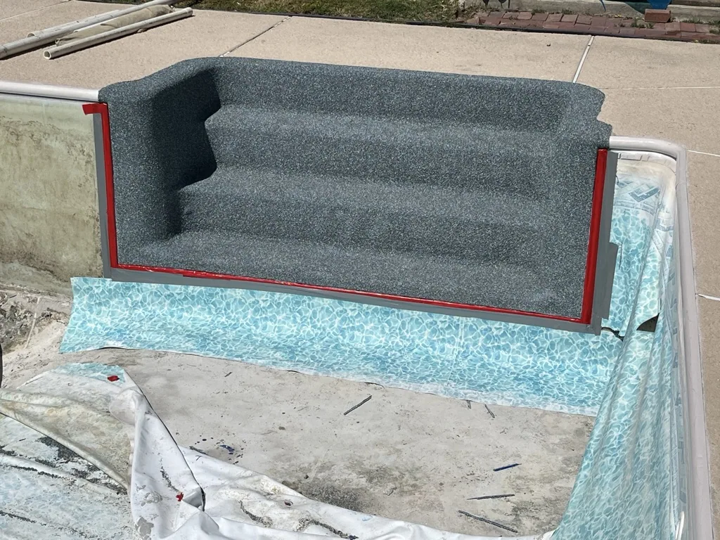 Gray upholstered couch with red frame placed in dumpster against concrete surface
