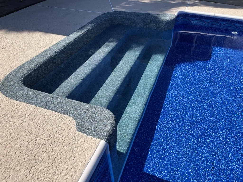 Swimming pool steps leading into blue water with concrete decking and sun shadows