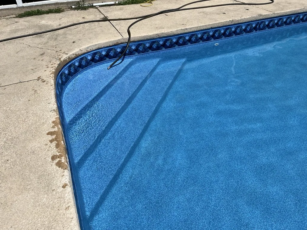 Swimming pool with blue interior and decorative border next to concrete deck with black hose