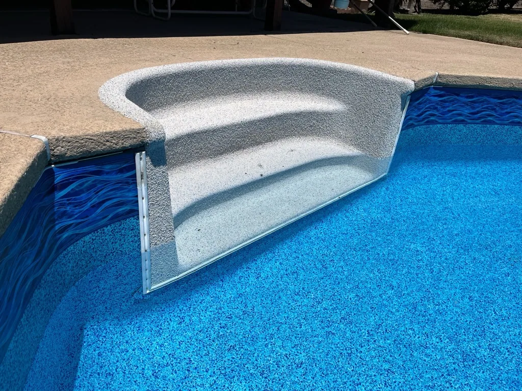 Concrete sun shelf and bench seat in swimming pool with bright blue plaster and dark wave pattern pool lining