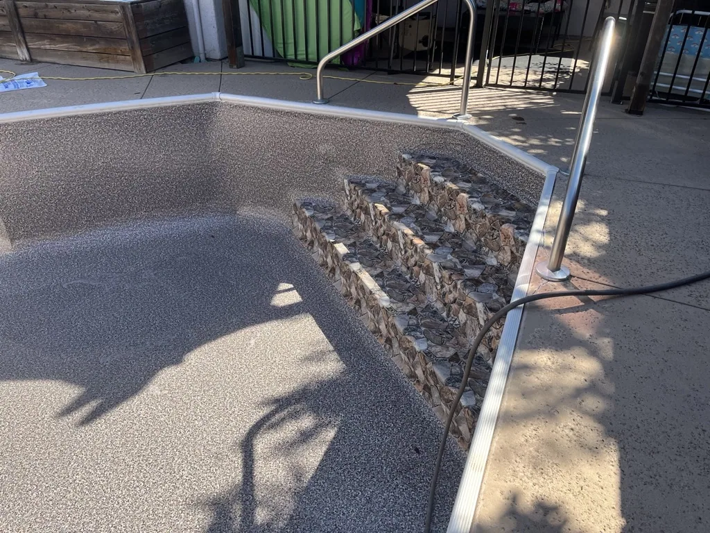 Empty pool with concrete deck and stone accent wall, metal handrail visible, outdoor commercial setting