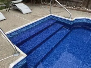 Swimming pool with blue tile interior and entry steps, surrounded by concrete deck and lounge chairs