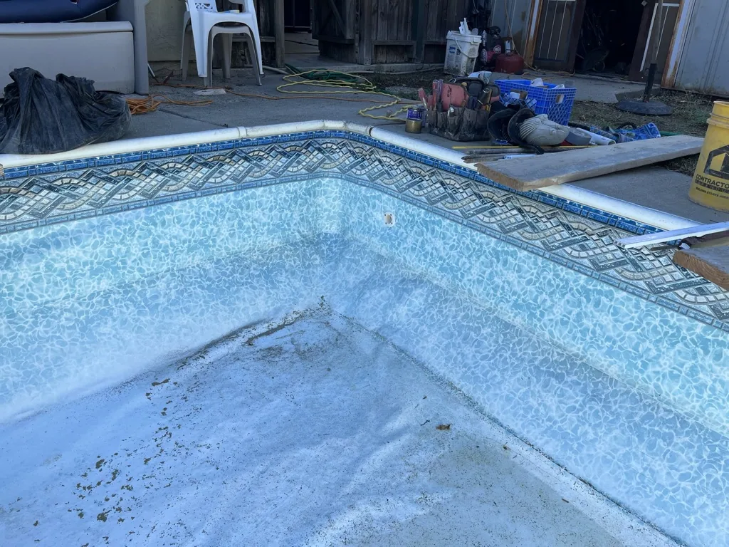Empty swimming pool during renovation with blue tile walls and mesh cover, construction materials and equipment visible in background