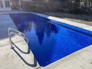 Residential rectangular swimming pool with blue tile interior and metal ladder on concrete deck
