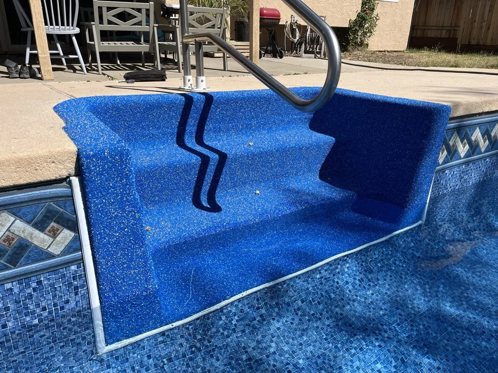Swimming pool with blue plaster finish, ladder, and surrounding patio area with white chairs