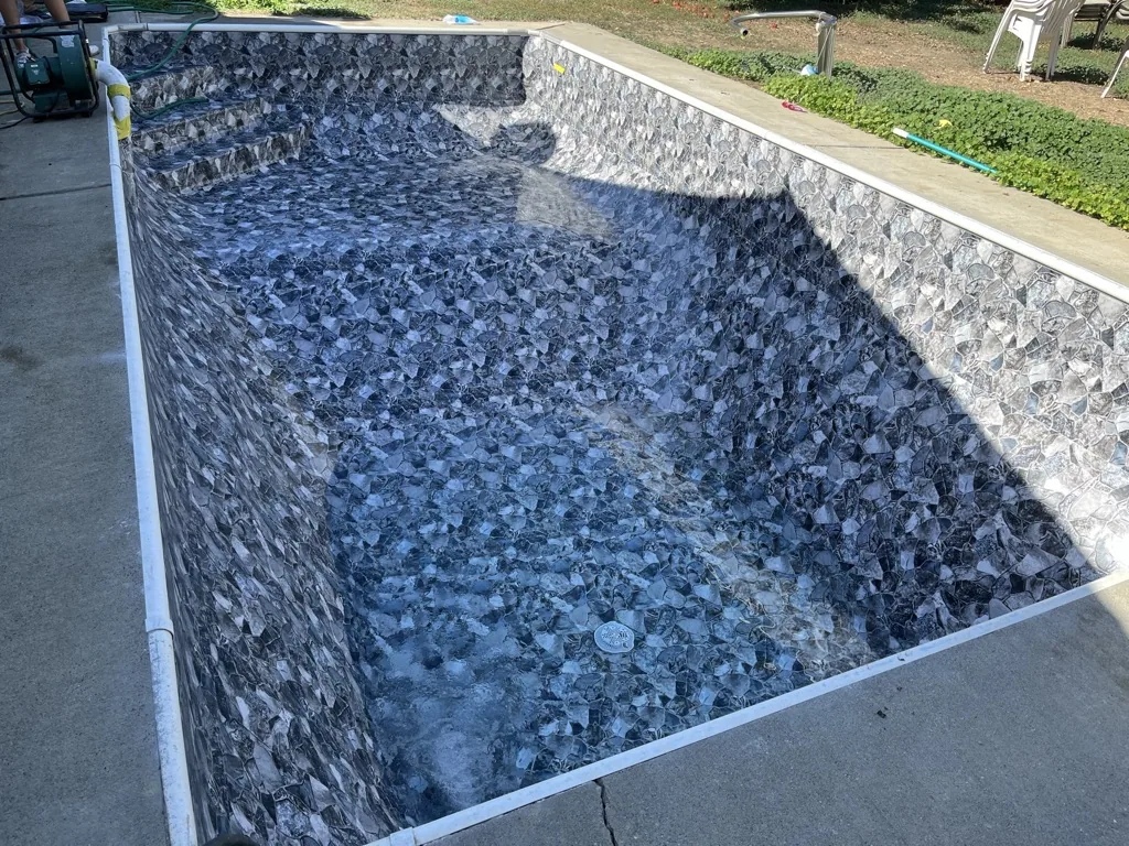 Empty in-ground swimming pool with blue stone texture lining and concrete deck surrounding it