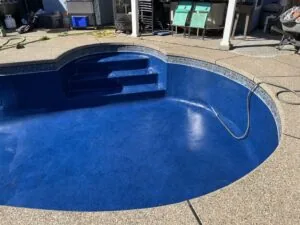 Empty blue fiberglass swimming pool with steps during maintenance or renovation, surrounded by concrete deck and residential buildings