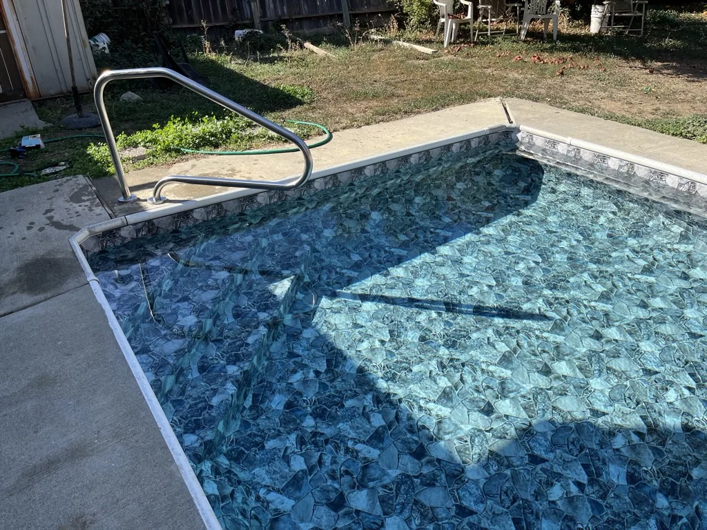 In-ground swimming pool with blue tile finish, metal ladder, and concrete deck in residential backyard