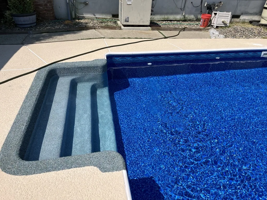 Swimming pool with blue water and concrete deck steps, surrounded by patio and residential equipment