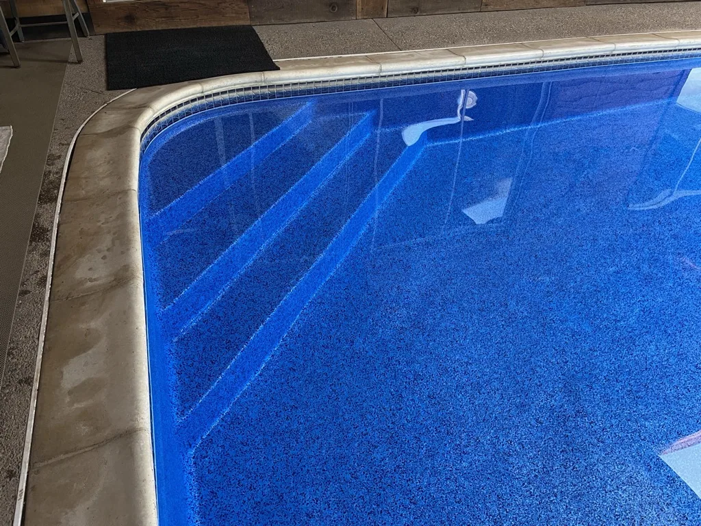 Swimming pool with blue textured interior, metal trim edge, and stair treads visible in shallow end