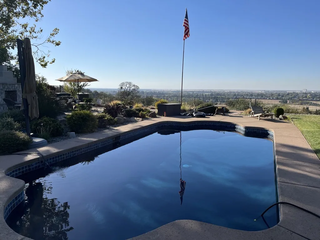 Swimming pool reflecting sky with American flag on hillside overlooking valley landscape