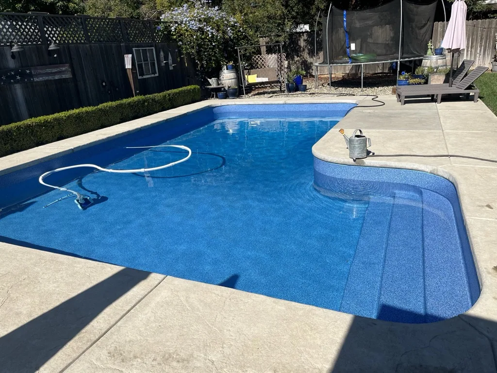 Backyard in-ground swimming pool with blue water and concrete deck, surrounded by landscaping and residential structures.