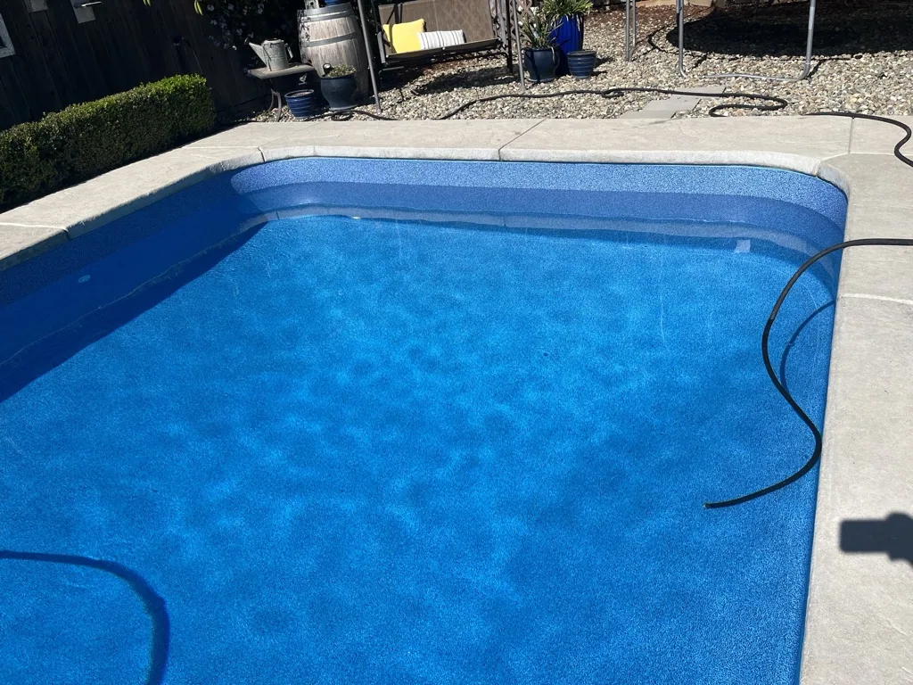 Blue in-ground swimming pool with concrete deck and surrounding landscape