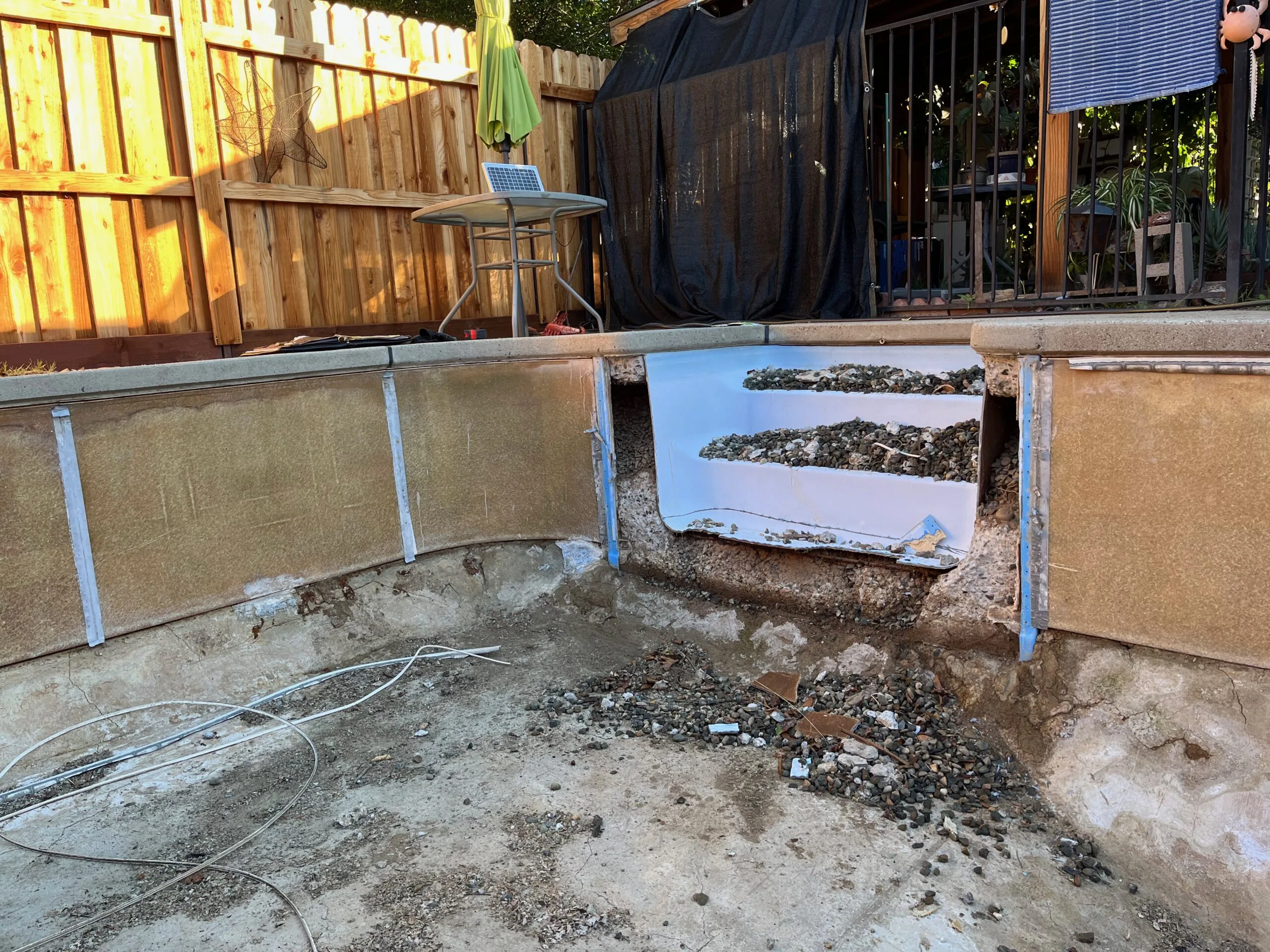 Outdoor concrete pool basin under construction with metal frame walls and collected gravel piles in backyard setting