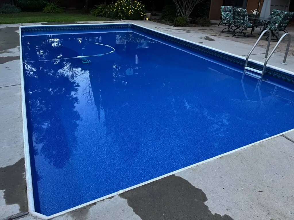 Empty rectangular swimming pool with bright blue water and metal ladder, surrounded by concrete deck and lounge chairs