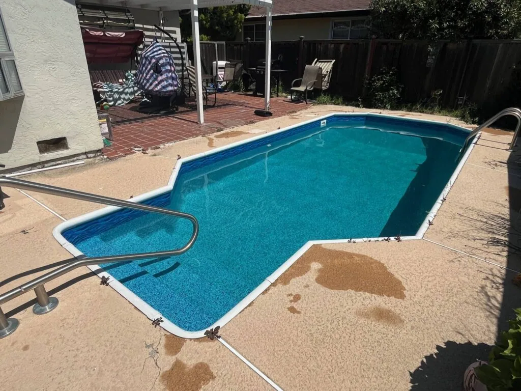 Residential backyard swimming pool with blue water, concrete deck, and patio area surrounded by fencing