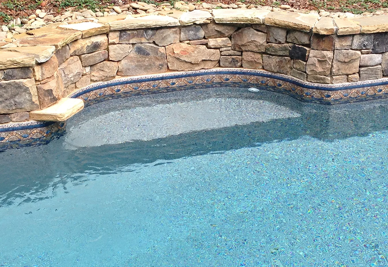 Curved inground swimming pool with turquoise water and decorative stone and tile border