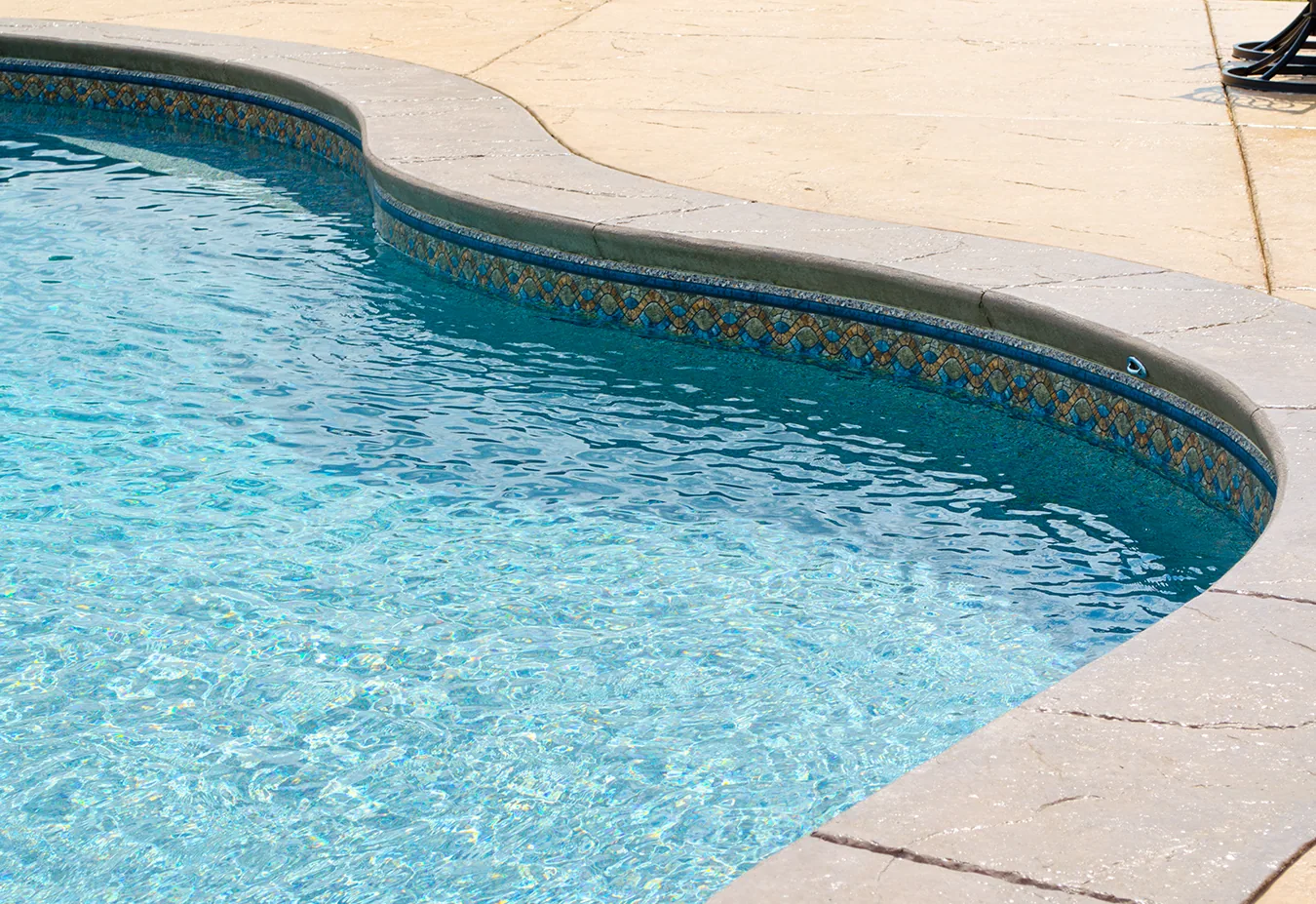 Curved swimming pool with clear blue water and decorative tile border beside concrete deck