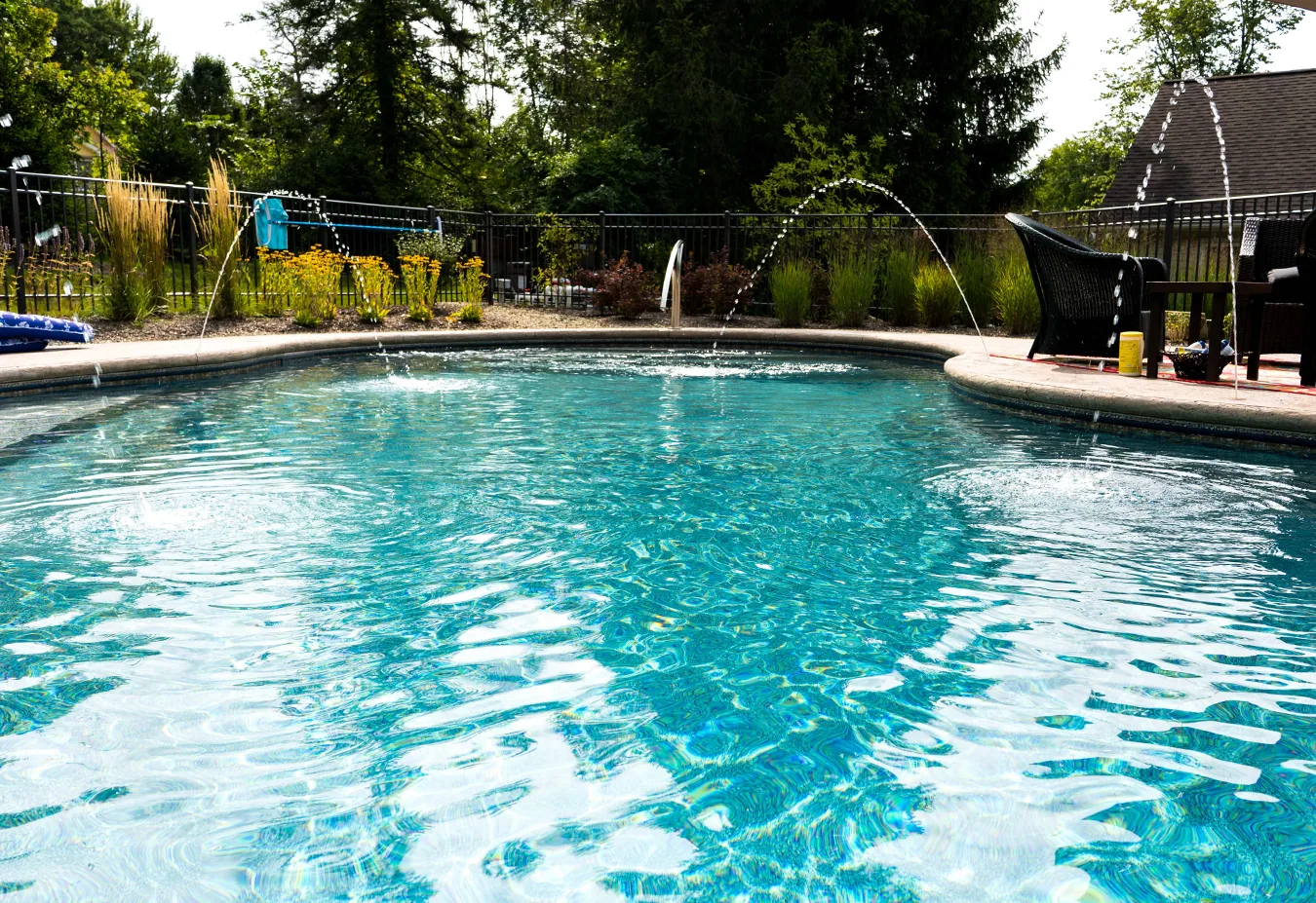 Turquoise inground swimming pool with curved water features and black safety fencing, surrounded by landscaping and trees